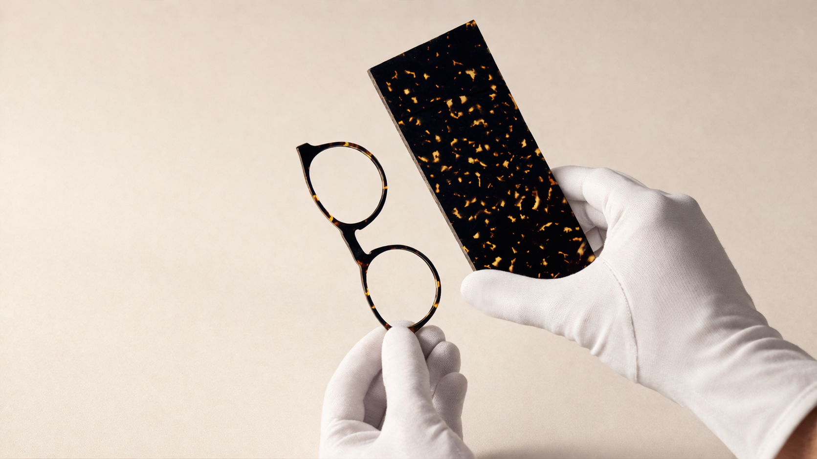 White-gloved hands holding raw acetate block and finished tortoiseshell frame.