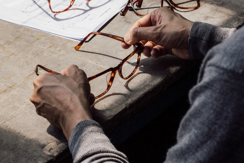Hands holding tortoise frames over technical drawings